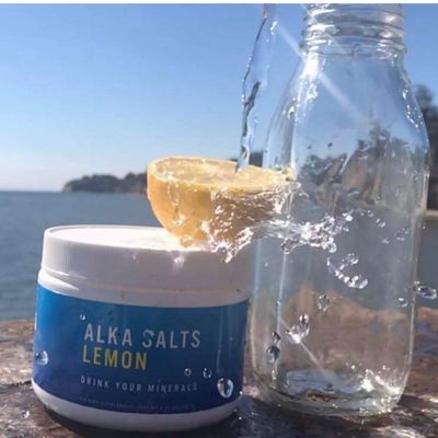 A jar of Alka Salts by the ocean with water splashing over a lemon